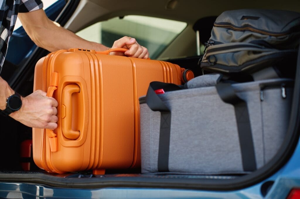 Man loading suitcase into car trunk, Packing luggage for travel