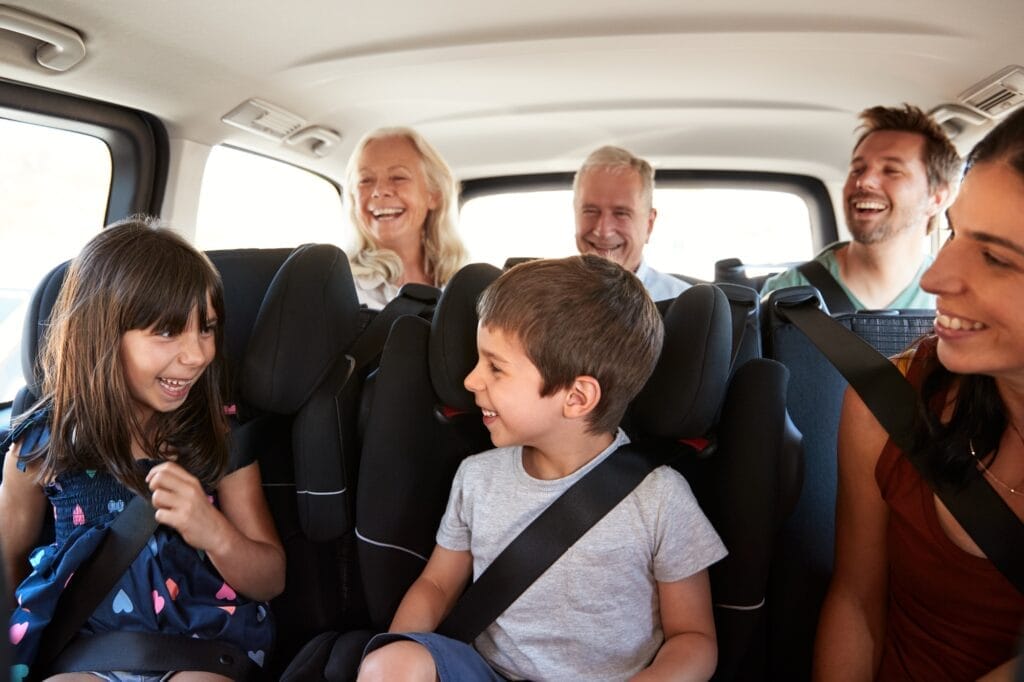 Three generation white family sitting in two rows of passenger seats in a car, looking at each other